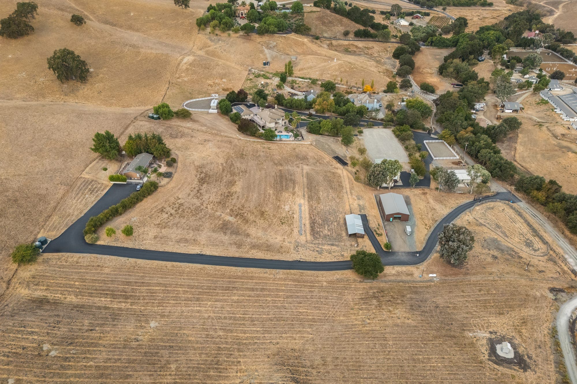Aerial view of the long paved drive crossing the open acreage toward the shop and barn.