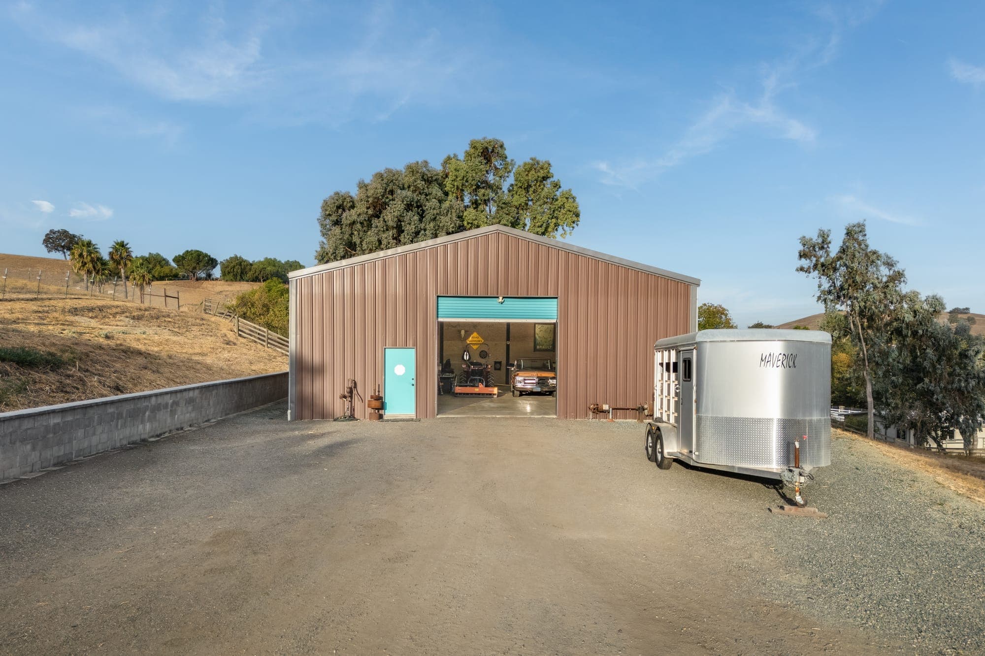 Front of the 2,400 sq ft shop with its oversized roll-up door open, a horse trailer parked beside it.