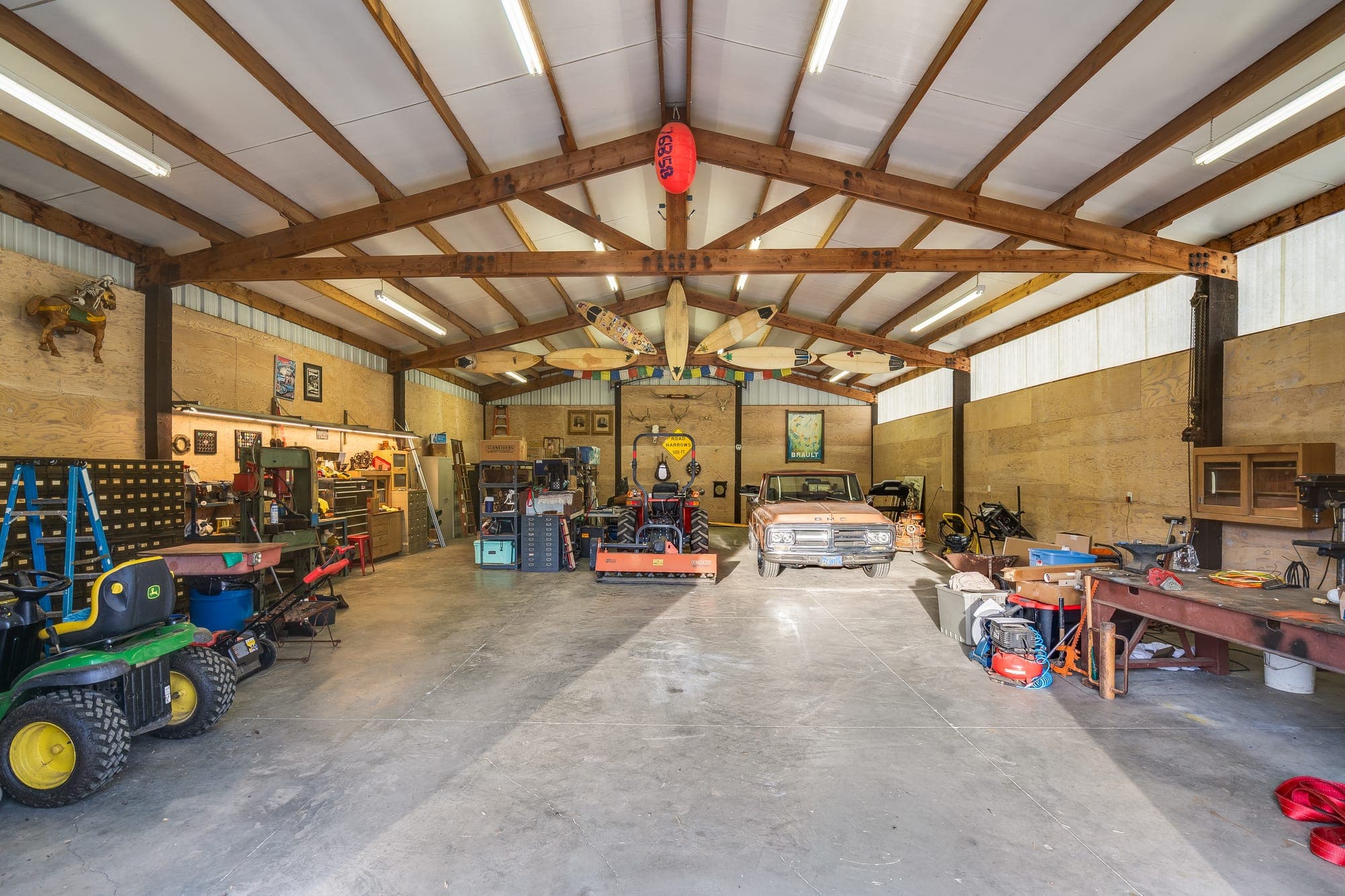 Inside the insulated shop: tall ceilings, exposed beams, overhead lighting, and room for vehicles and equipment.