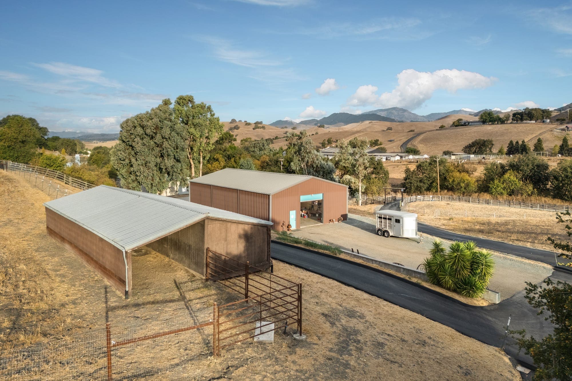 Aerial view of the covered barn with its pipe-panel pens beside the drive, the shop just beyond.