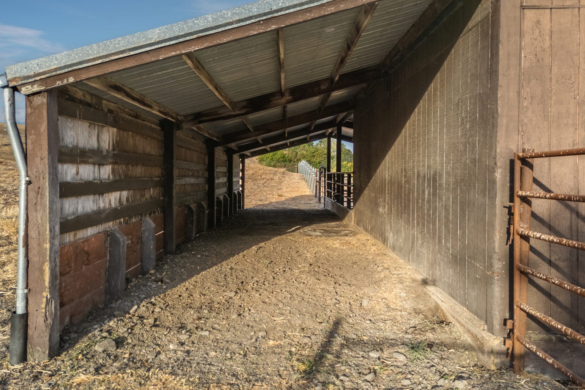 Looking down the barn's covered breezeway between wood walls toward the pasture.