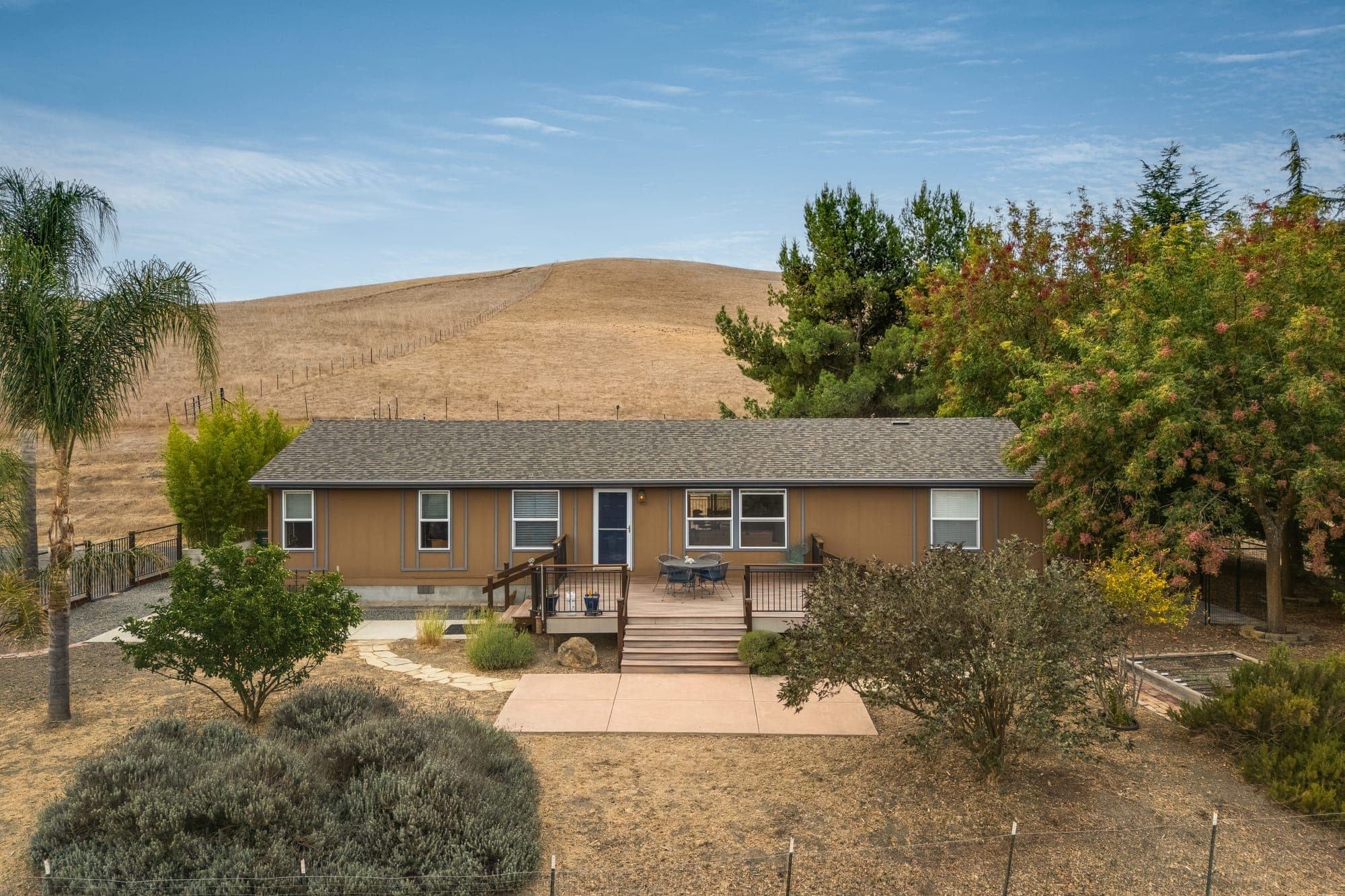 The single-story residence with its front deck and patio, surrounded by mature trees and the hills.