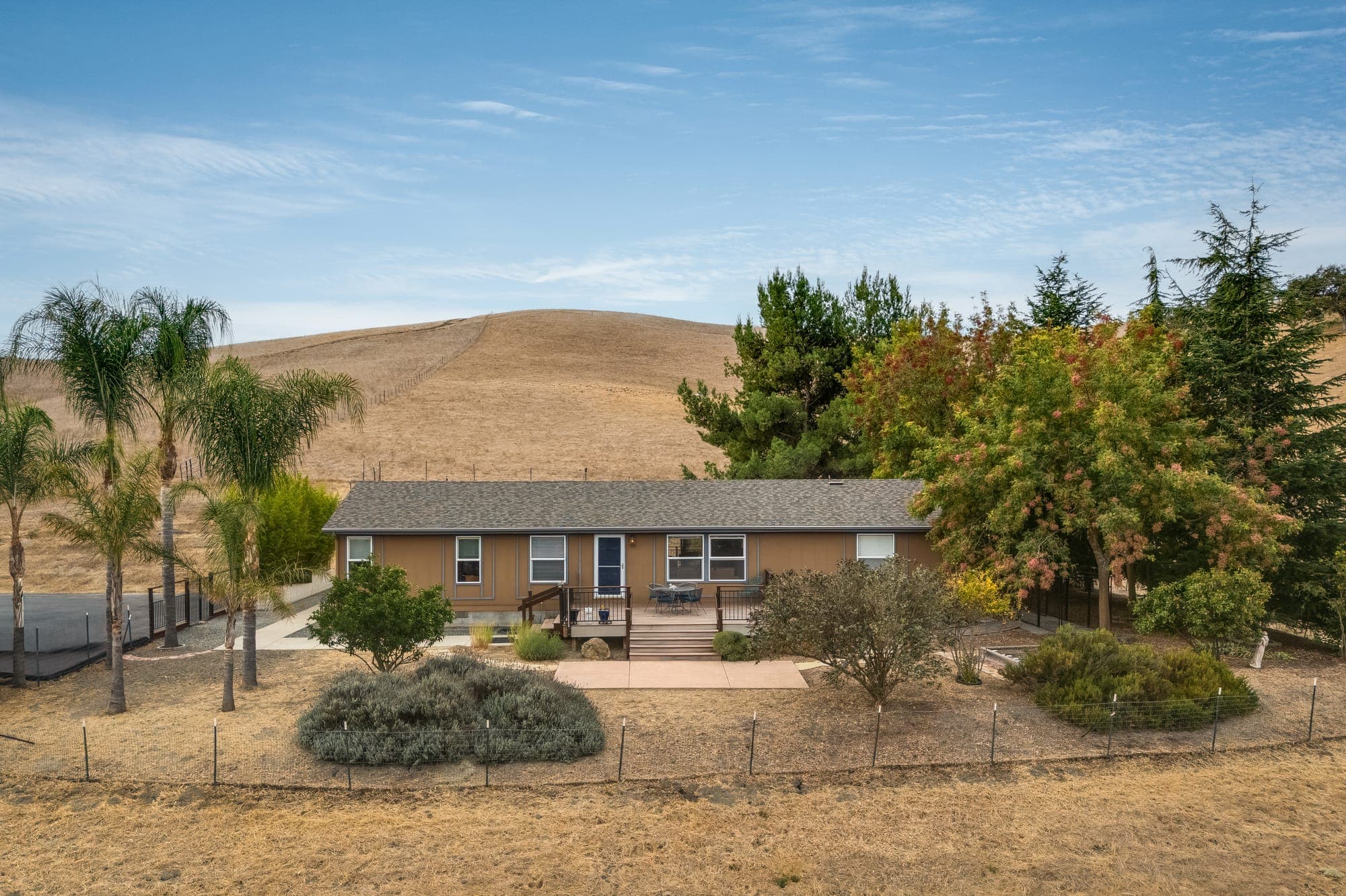 The residence among palms and mature trees with a hillside behind.