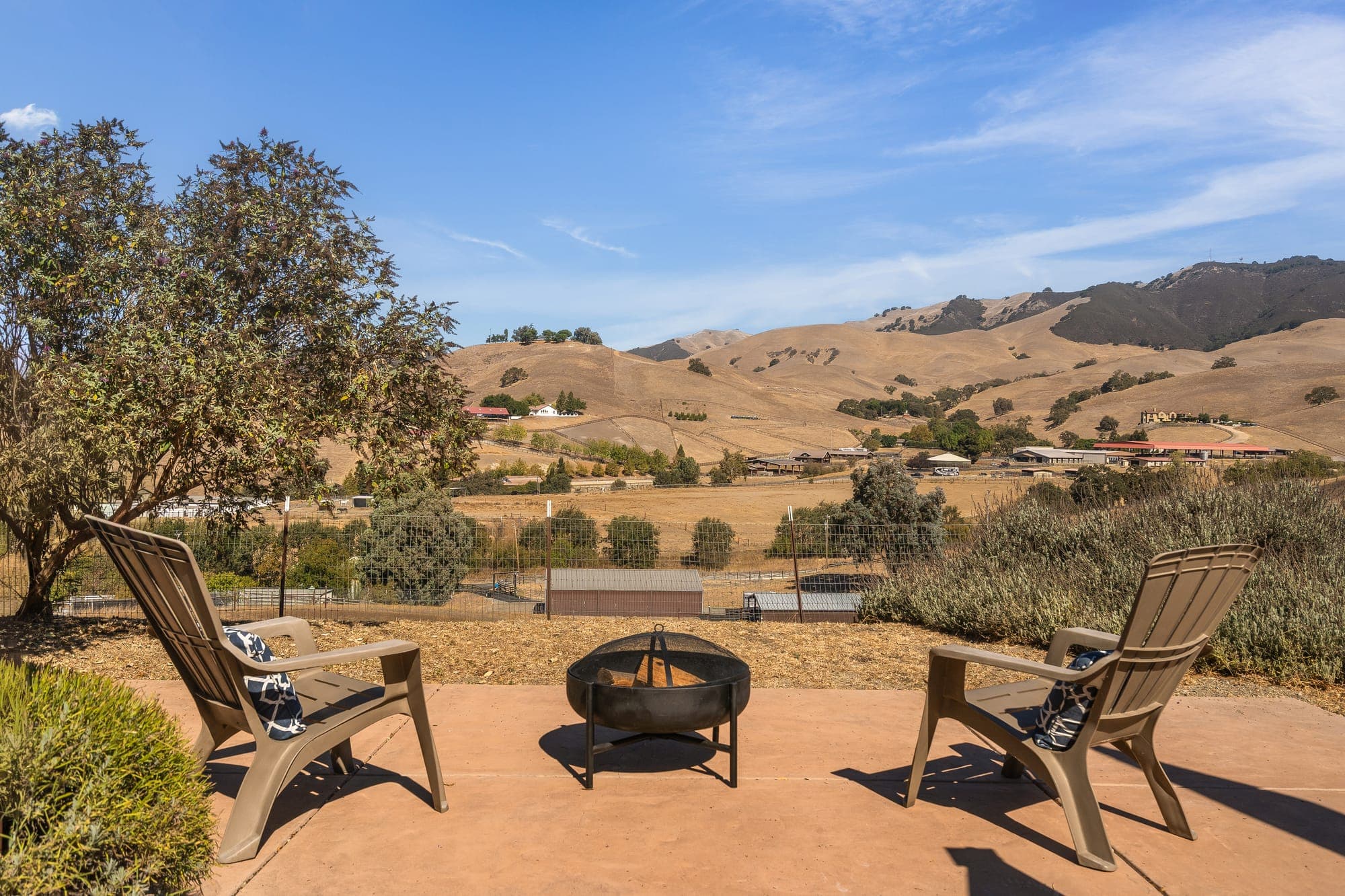 Chairs around a fire bowl on a patio overlooking the valley and hills.
