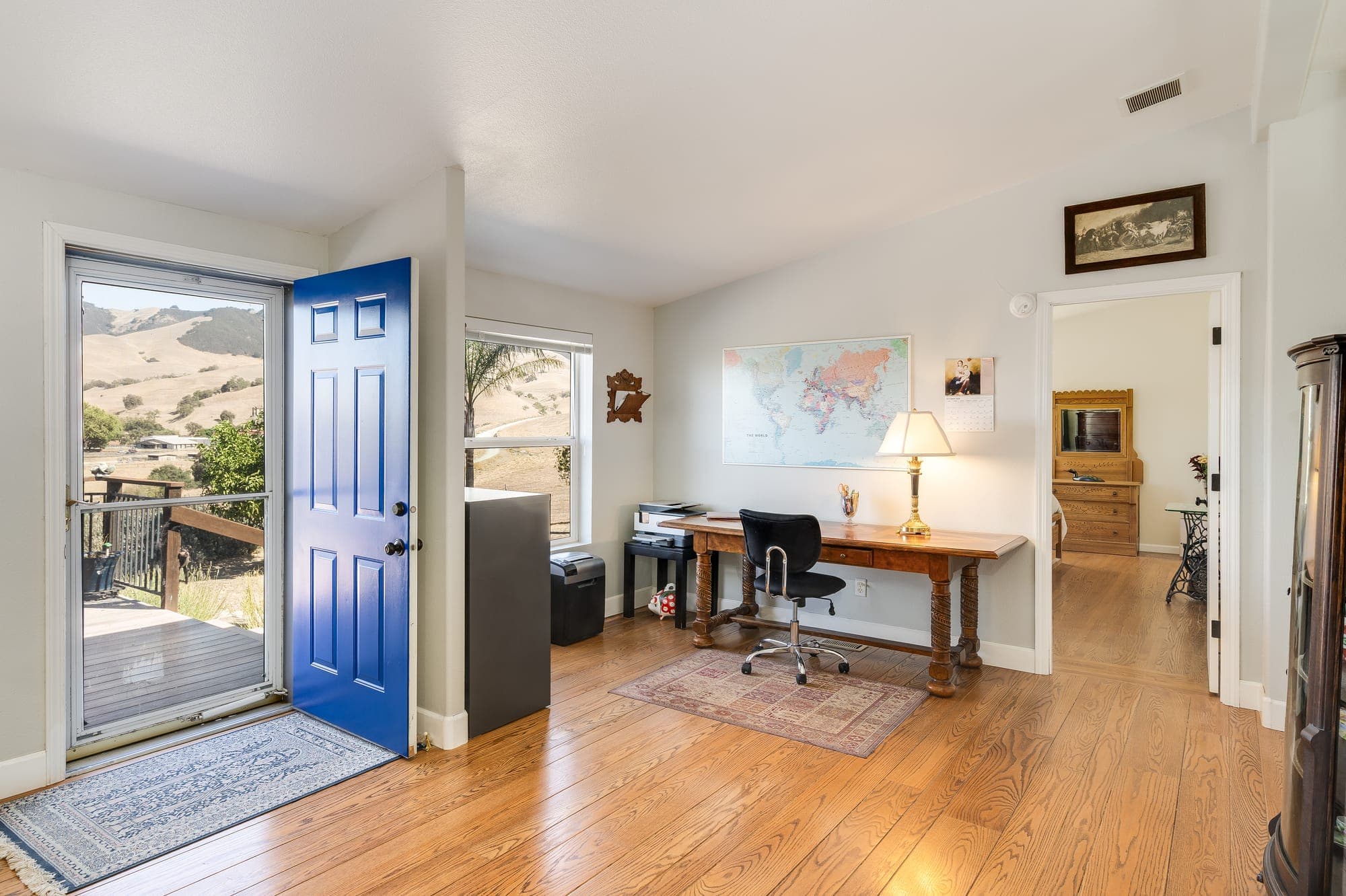 A bright room with a desk by the front door and hill views through the windows.