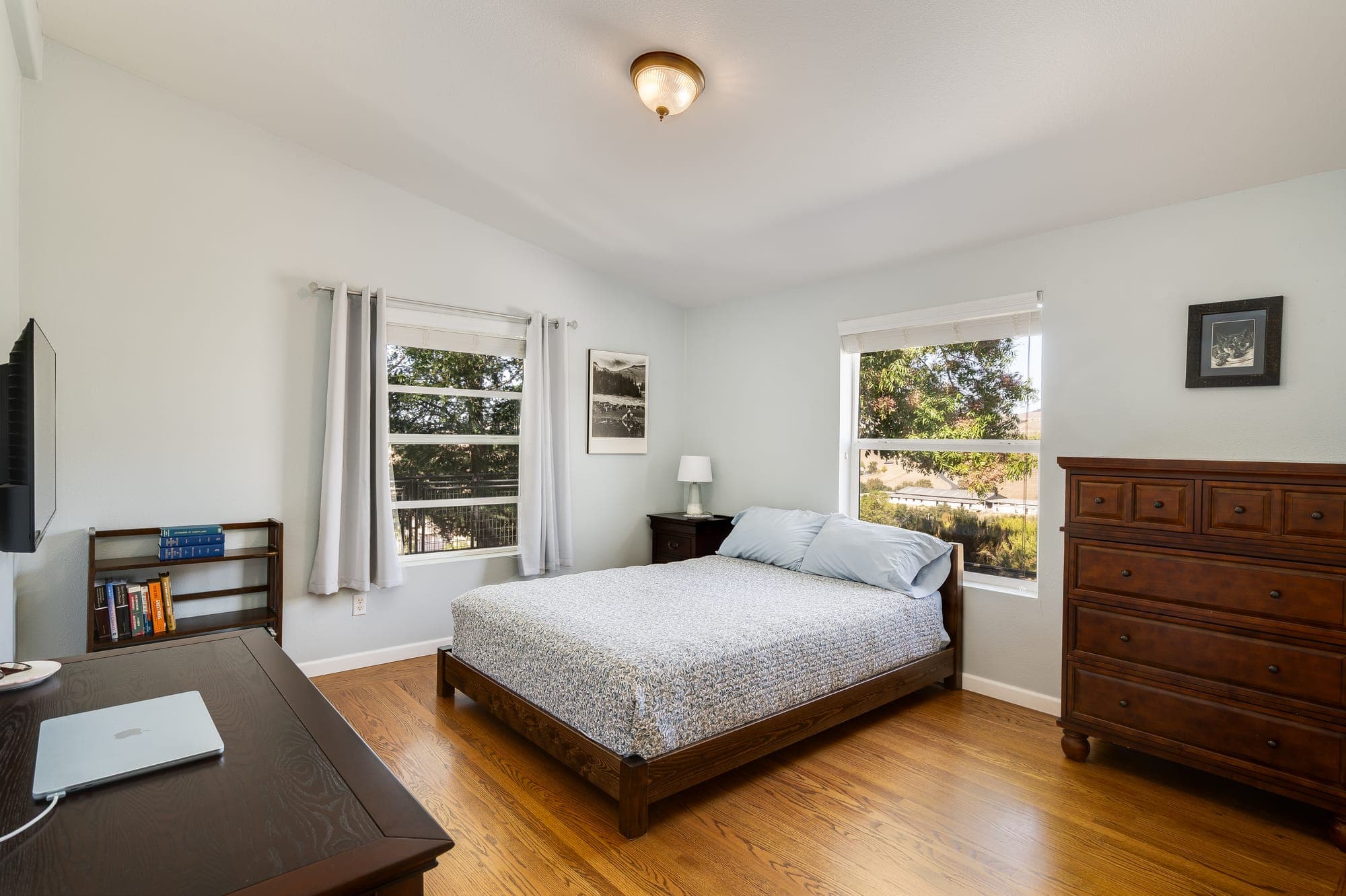 A bedroom with two windows and wood floors.