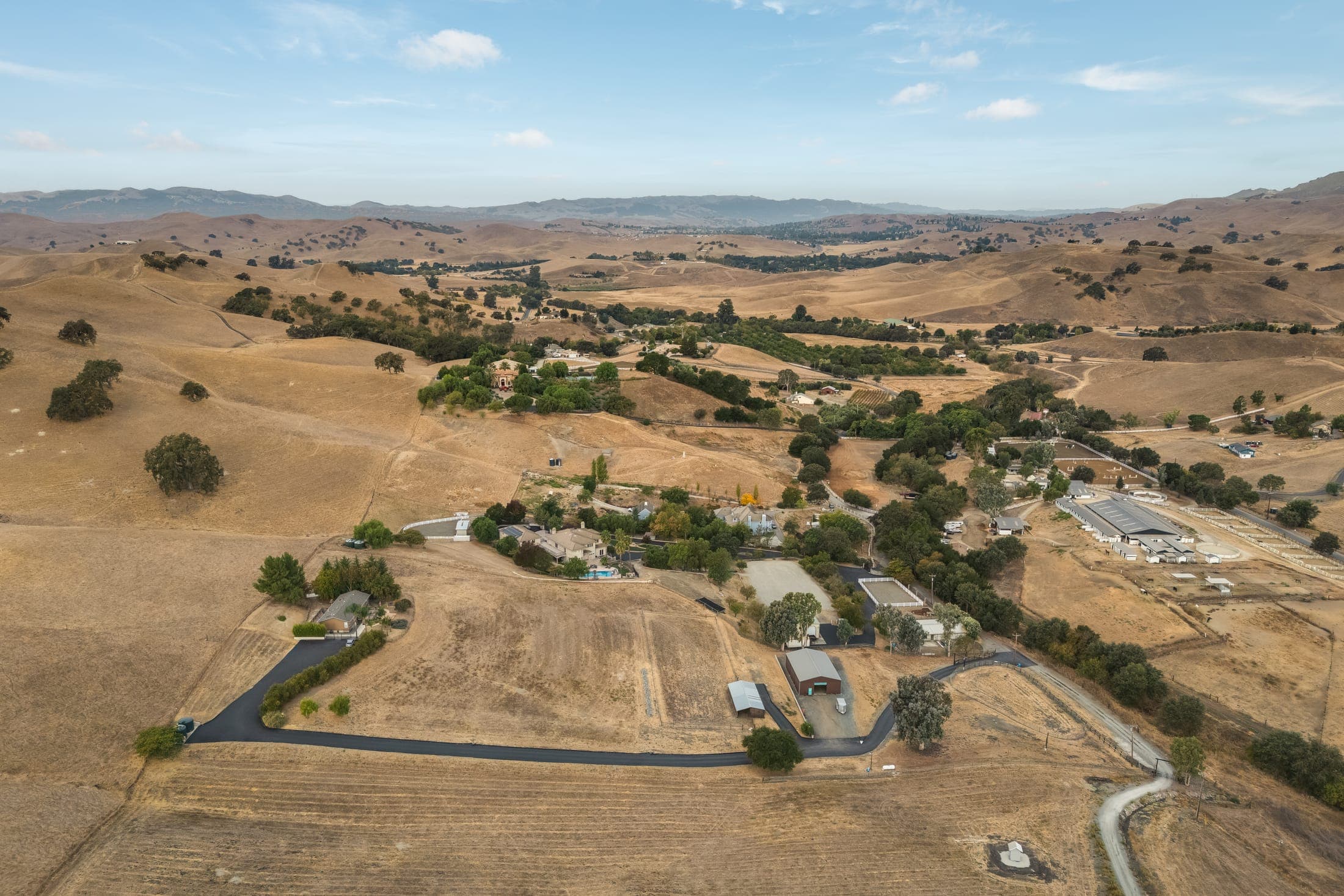 Aerial view of the property's drive winding across open land toward the residence and outbuildings.
